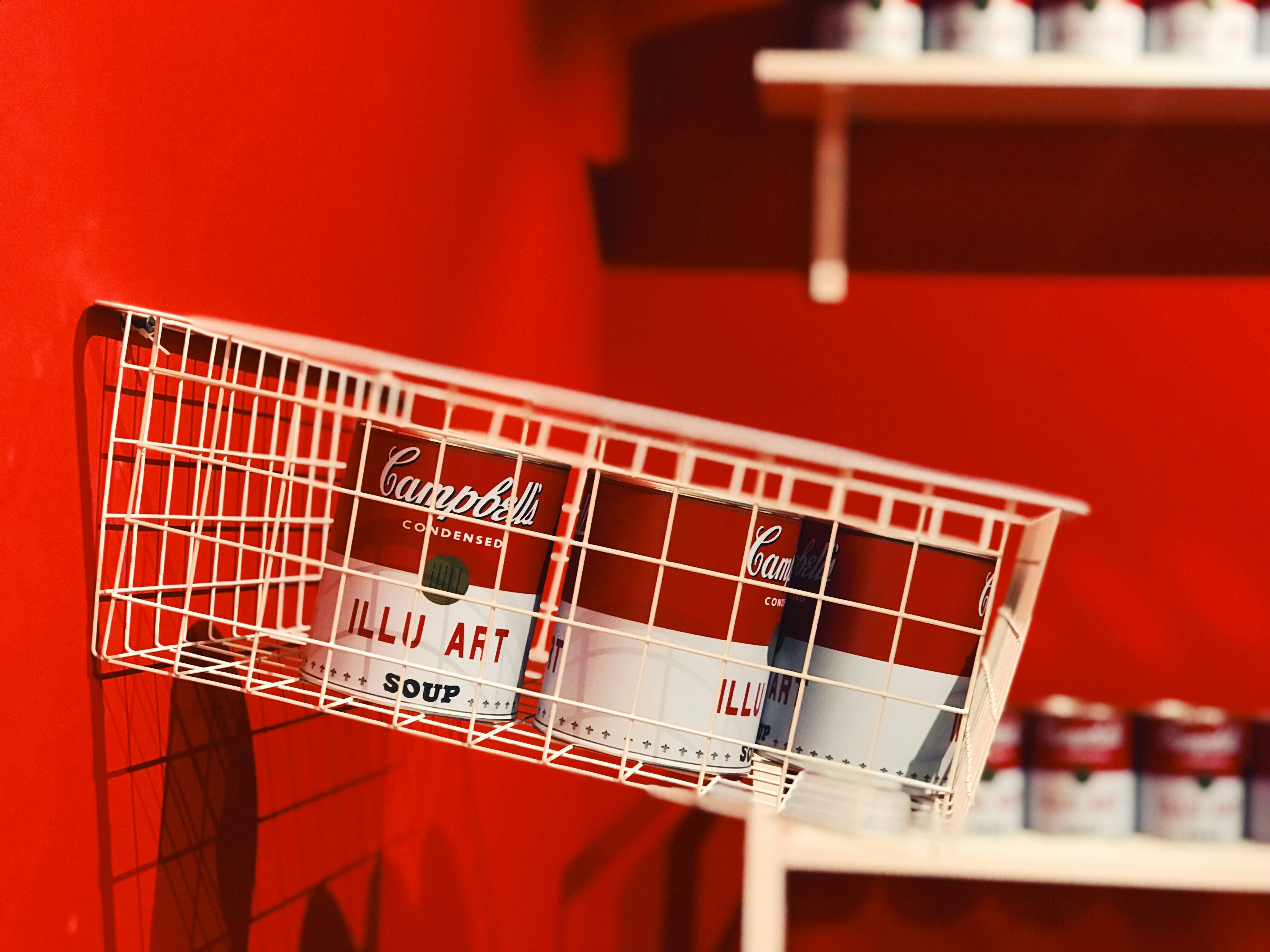 a red wall with a white wire basket holding cans of coca - cola